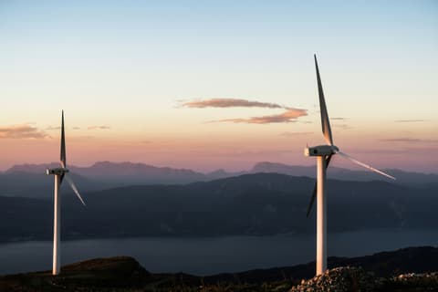 Two wind turbines on a ridge at sunset above mountains and sea